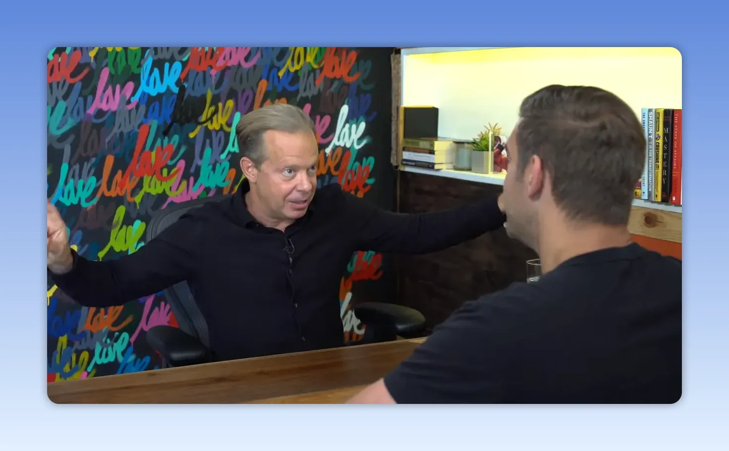 Intervenant en entretien, bras étendus pour illustrer l'amplification du cœur, mur coloré 'love' en arrière-plan