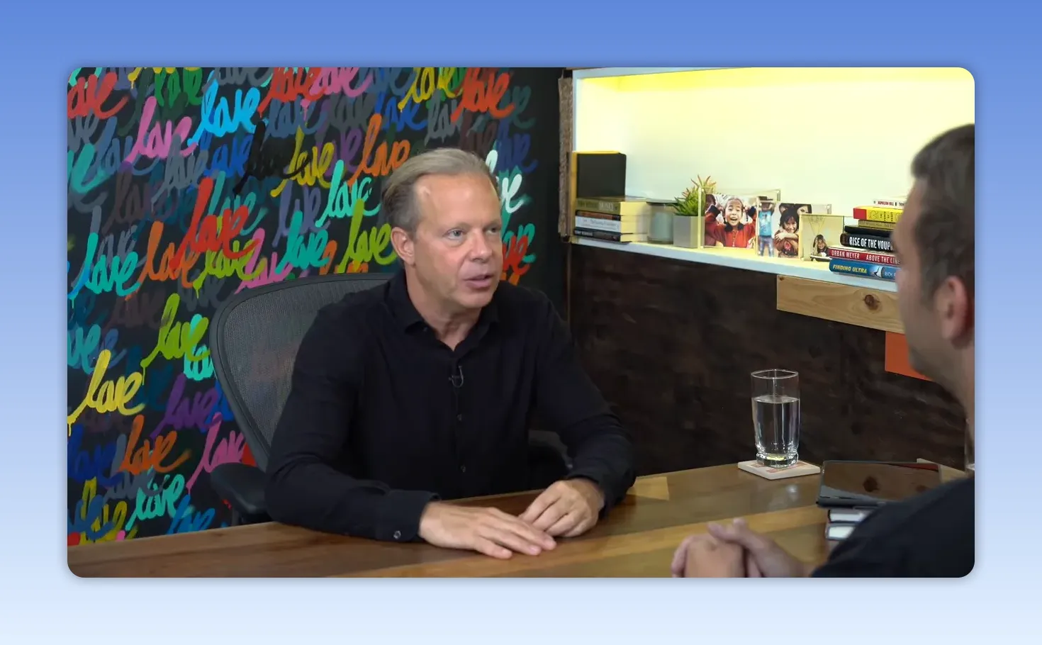 Plan large d'un intervenant parlant à son interlocuteur, décor mural coloré 'love' et verre d'eau sur la table