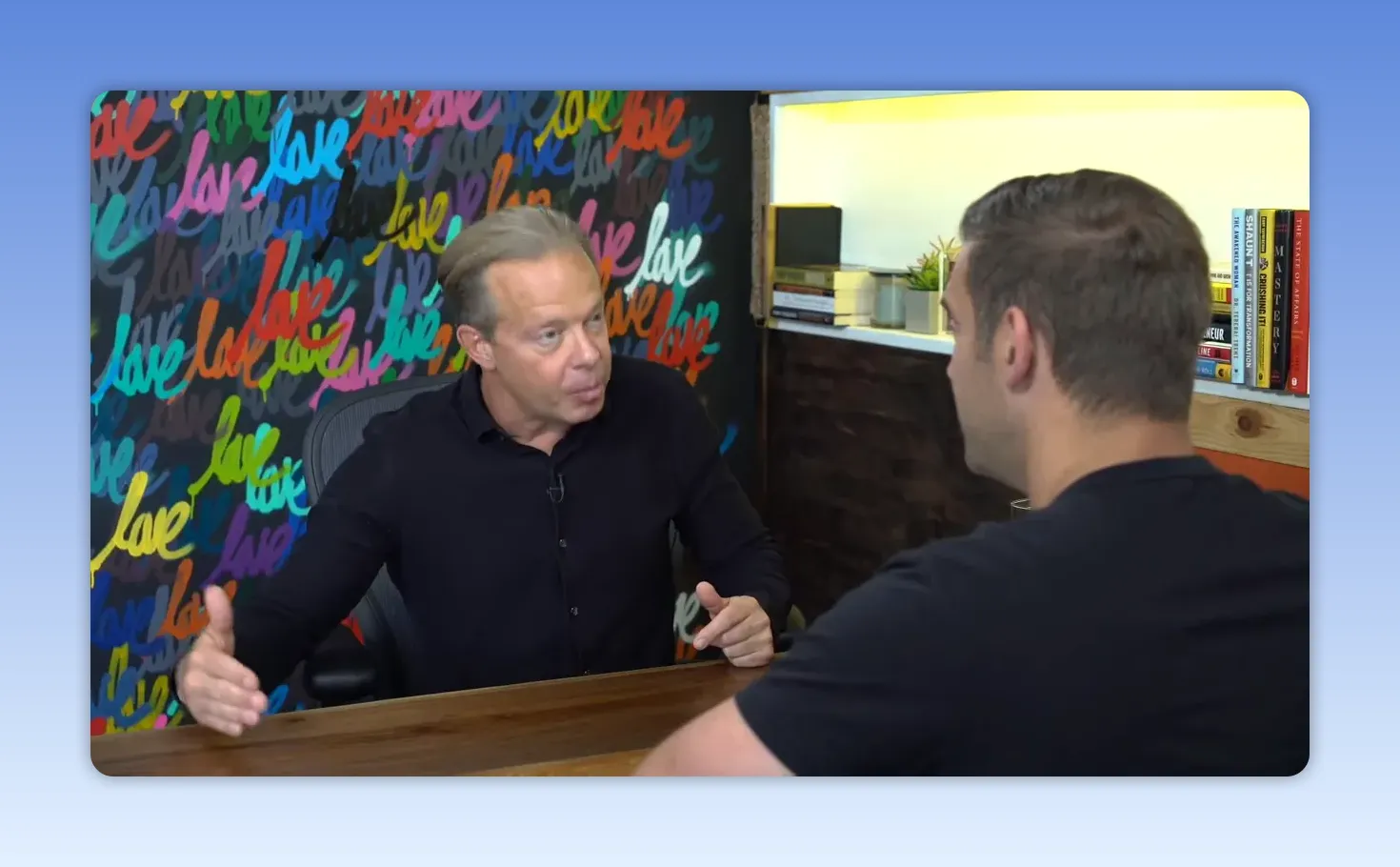 Deux personnes en interview à une table, l'un expliquant avec gestes la connexion esprit-corps.