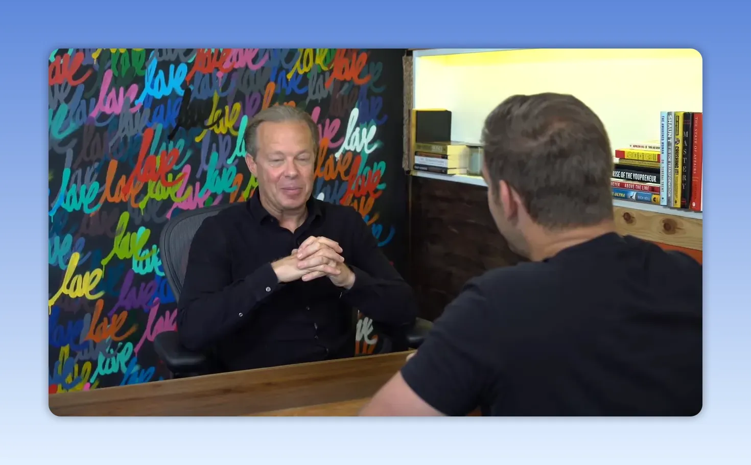 Intervenant, mains jointes, regard posé et expression réfléchie devant un mur coloré 'love'